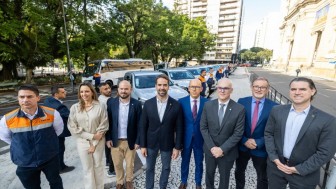 Grupo composto por representantes do MPSP, Defesa Civil e Governo RS posa para a foto, com uma fileira das novas viaturas ao fundo