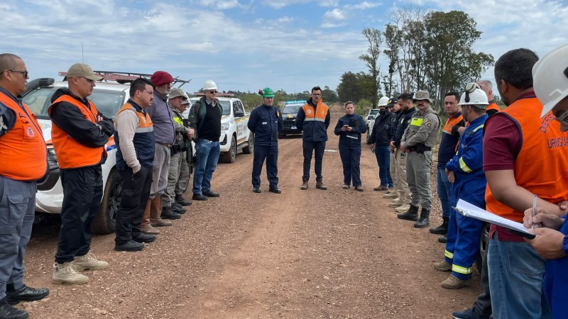 Um grupo de pessoas est&aacute; reunida em roda, em uma estrada de barro. &Eacute; poss&iacute;vel verificar pelas vestimentas que participam de diferentes &oacute;rg&atilde;os, como da Defesa Civil, da Brigada Militar e companhia de g&aacute;s.